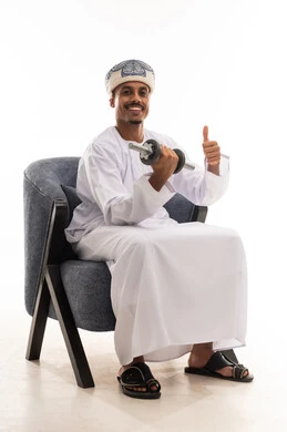 Raising the thumb up is a sign of feeling happy. An Arab Gulf Omani man wearing a white dishdasha and a turban is lifting heavy weights, feeling joy and physical strength. Portrait with a white background, full body.