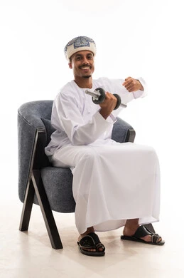 Portrait with a white background, full-body, an Arab Gulf Omani man wearing a turban and a white dishdasha, lifting heavy weights to build body muscles, raising his index finger and thumb towards the heavy weights, gestures of happiness, looking at the camera.