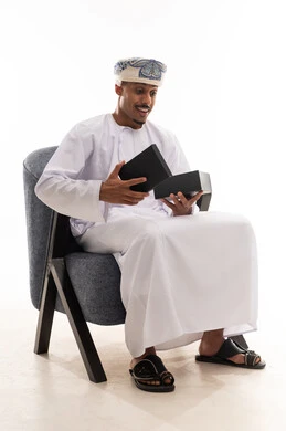 The feeling of happiness when opening a gift, an Arab Gulf Omani man wearing a white dishdasha and a turban looks at the gift box with joy, portrait with a white background, full body.