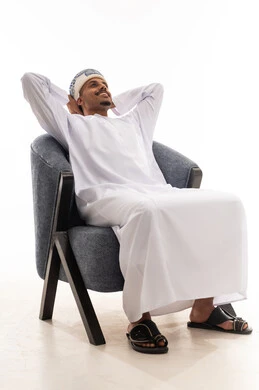 وضع قبضة اليدين خلف الرأس اشارة الى الاستجمام و الشعور بالراحة , رجل عربي خليجي عماني يرتدي دشداشة بيضاء و العمامة يجلس على كرسي رمادي , النظر للاعلى الى شئ ما , بورتريه خلفية بيضاء , الجسم بالطول الكامل