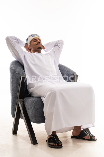 الجلوس على الكرسي الرمادي المريح و استنشاق النسيم العليل و الرائحة الجميلة , رجل عربي عماني خليجي يرتدي دشداشة بيضاء و العمامة يثني ذراعيه خلف الرأس يشعر بالاستجمام و الراحة , بورتريه خلفية بيضاء , الجسم بالطول الكامل