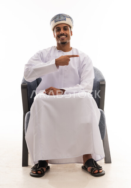 رجل عربي خليجي عماني يرتدي دشداشة بيضاء و عمامة يشير باصبع السبابة الي الجانب , النظر الى الكاميرا , بورتريه خلفية بيضاء , الجسم بالطول الكامل