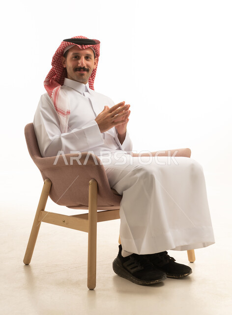 رجل سعودي بالثوب التقليدي يجلس في استوديو بخلفية بيضاء