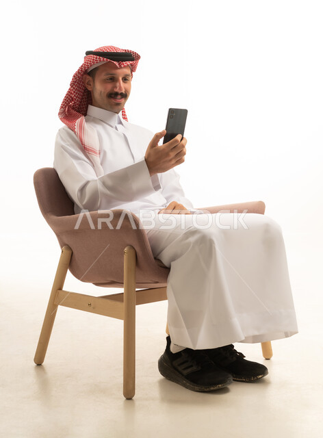 رجل سعودي بالثوب التقليدي يستخدم الهاتف الذكي