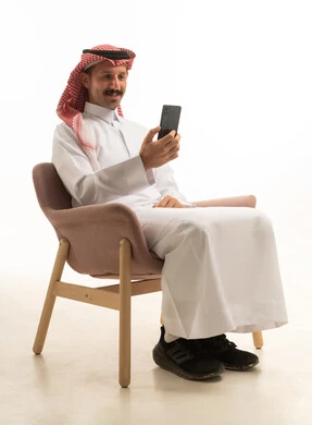 رجل سعودي بالثوب التقليدي يستخدم الهاتف الذكي