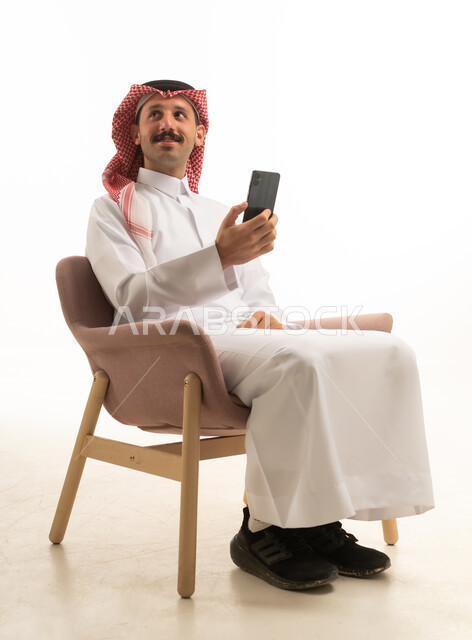 رجل سعودي بالزي التقليدي يستخدم هاتف ذكي في استوديو