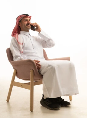 رجل سعودي يتحدث بالهاتف جالساً بخلفية بيضاء