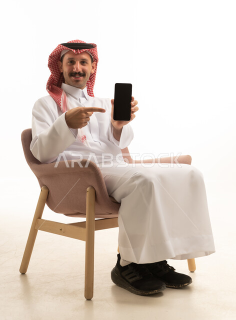 رجل سعودي يشير إلى شاشة هاتف ذكي بخلفية بيضاء
