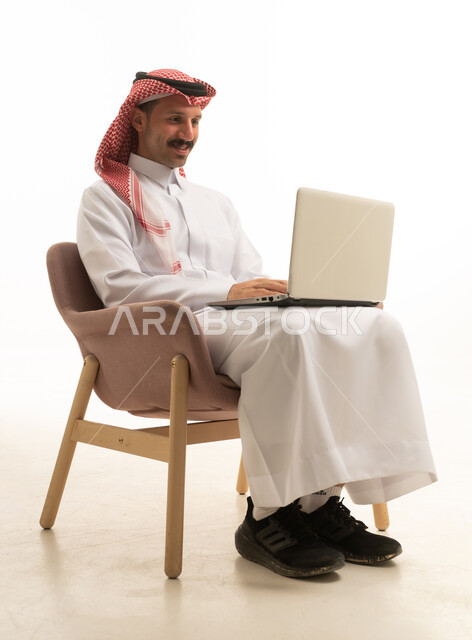 رجل سعودي بالزي التقليدي يستخدم الحاسوب المحمول خلفية بيضاء