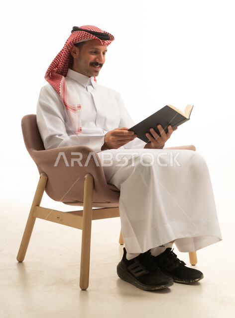 رجل سعودي بالزي التقليدي يقرأ كتاباً في الاستوديو