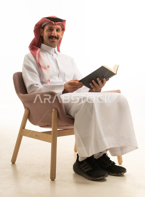 رجل سعودي يجلس على كرسي يقرأ كتاباً خلفية بيضاء