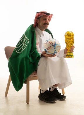 رجل سعودي يحمل كرة قدم وكأس البطولة بخلفية بيضاء