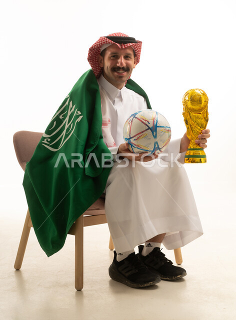 رجل سعودي يحمل كرة قدم وكأس مع العلم الوطني