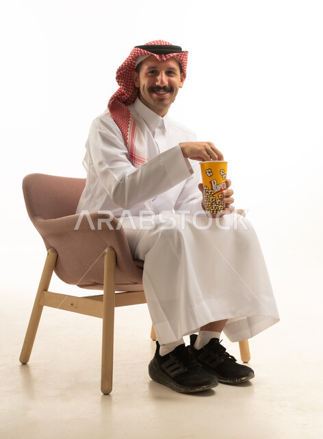 رجل سعودي بالزي التقليدي يأكل الفشار في الاستوديو