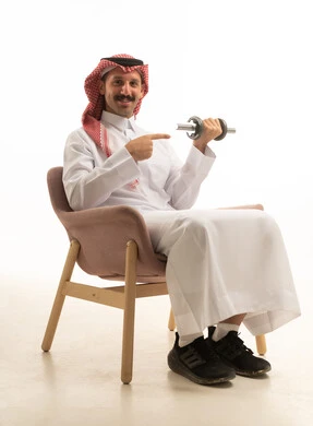 رجل سعودي بالزي التقليدي يمارس الرياضة بالدمبل