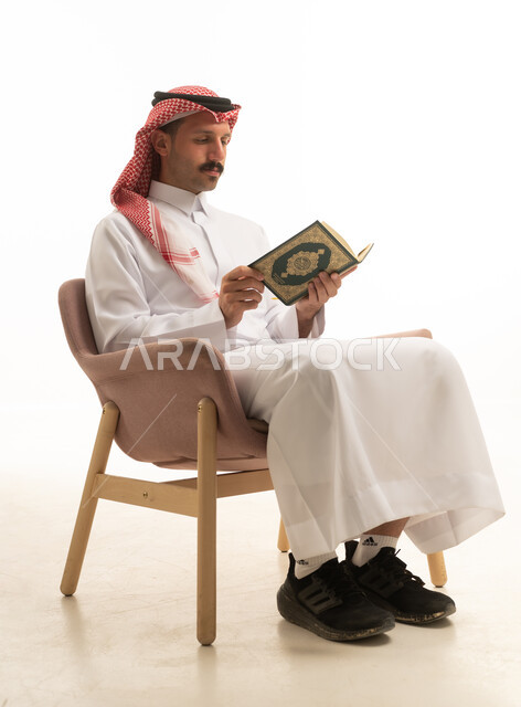 رجل سعودي يقرأ القرآن الكريم بخلفية بيضاء في استوديو