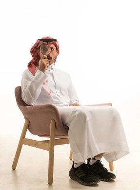 رجل سعودي يمسك عدسة مكبرة على خلفية بيضاء