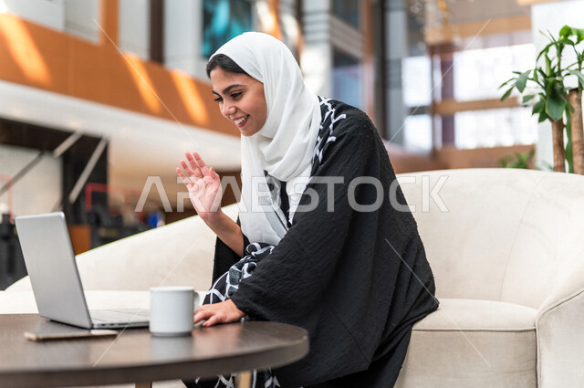 A Gulf Saudi woman inside the tourist hotel, using a laptop computer to accomplish tasks, the concept of technology and the use of modern technical devices, remote work, professions and jobs, work session, surfing the Internet, business trip, tourism and
