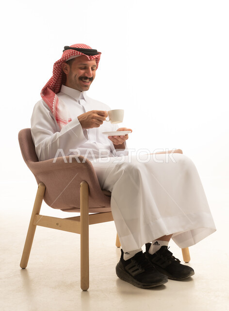 رجل سعودي بالزي التقليدي يمسك فنجان قهوة في استوديو