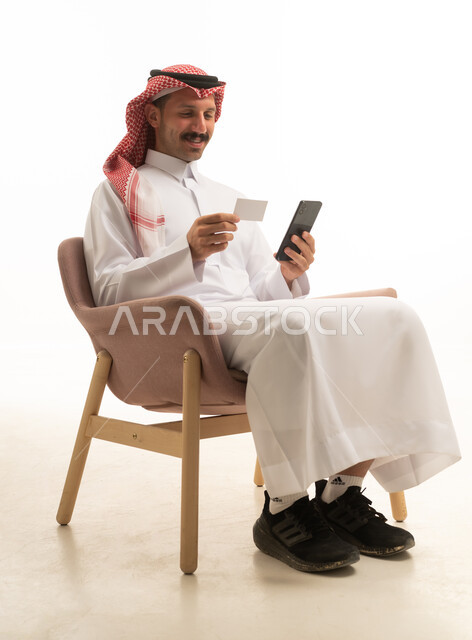 رجل سعودي يستخدم الهاتف والبطاقة الائتمانية على خلفية بيضاء