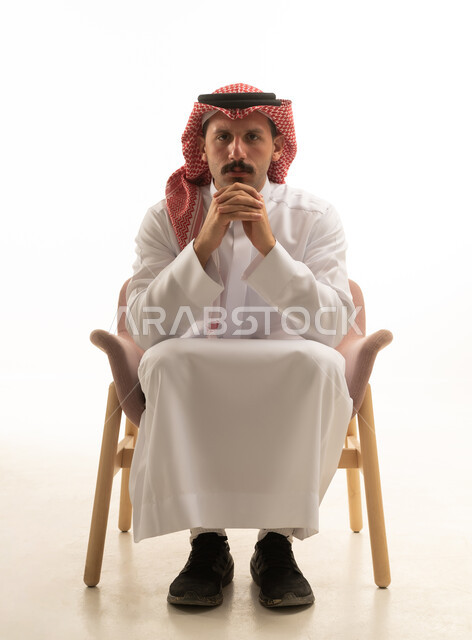 Saudi Man in Traditional Thobe Sitting in White Studio