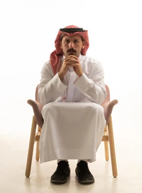 رجل سعودي يرتدي الثوب التقليدي يجلس في استوديو أبيض