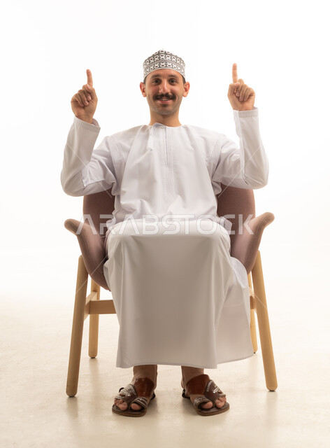 رجل سعودي يجلس على كرسي يشير للأعلى في استوديو