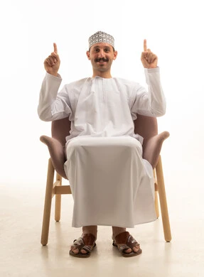 رجل سعودي يجلس على كرسي يشير للأعلى في استوديو