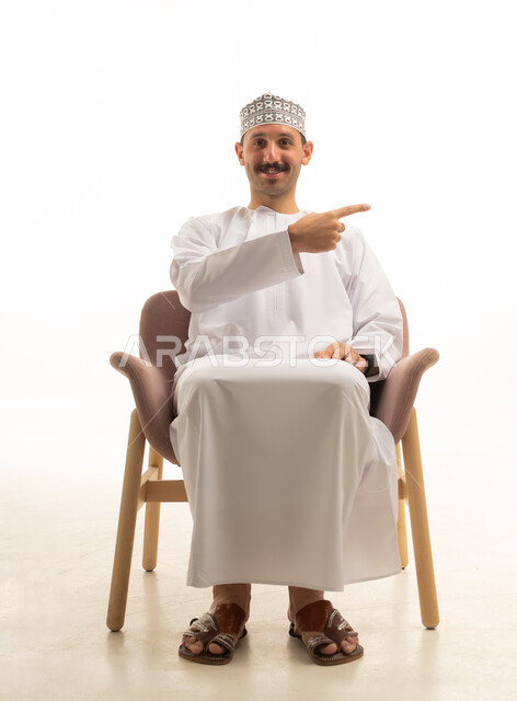 رجل عماني عربي خليجي يرتدي الكمه والدشداشه يجلس على كرسي بايماءات وحركات متنوعه, خلفيه بيضاء