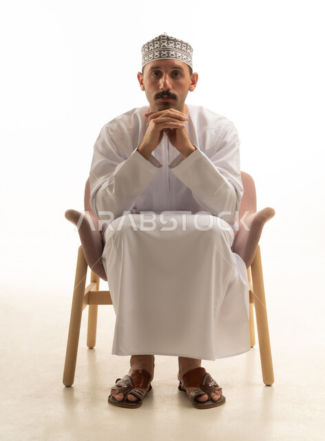 رجل سعودي بالثوب الأبيض التقليدي يجلس في استوديو