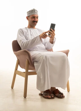 رجل عماني بالزي التقليدي يستخدم الهاتف الذكي