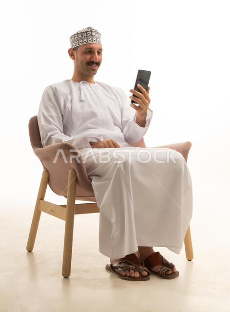 An Omani Arab Gulf man wearing a kumma and dishdasha is holding a mobile phone, sitting on a chair with various gestures and movements, against a white background.