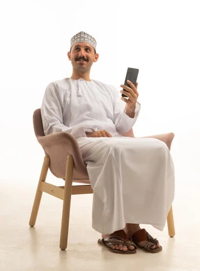 رجل عماني بالزي التقليدي يمسك هاتف ذكي