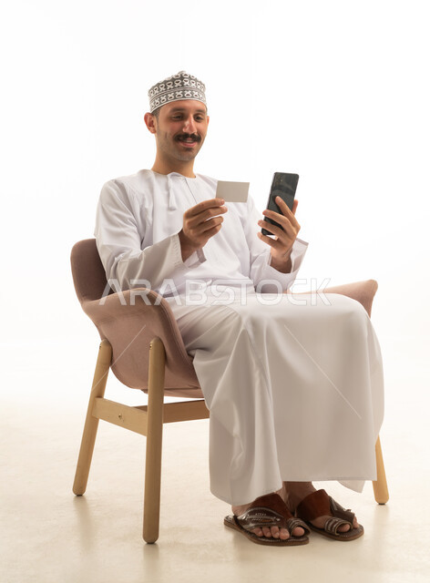 An Omani man using a phone and a credit card in a studio.