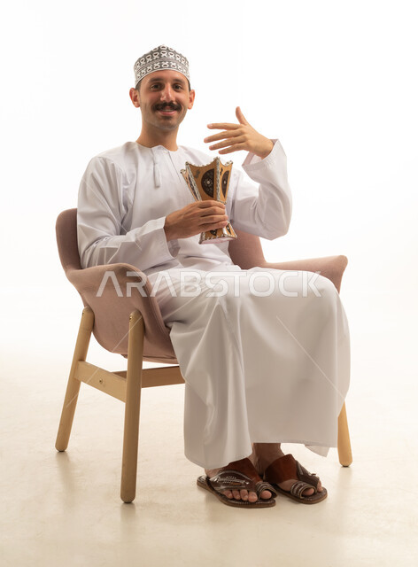An Omani man in traditional attire holding a incense burner in the studio.