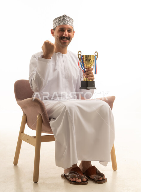 بورتريه لرجل عماني عربي خليجي يرتدي الدشداشه والكمه يجلس على كرسي يمسك بيده كاس الفوز, تشجيع الفريق الرياضي, خلفيه بيضاء