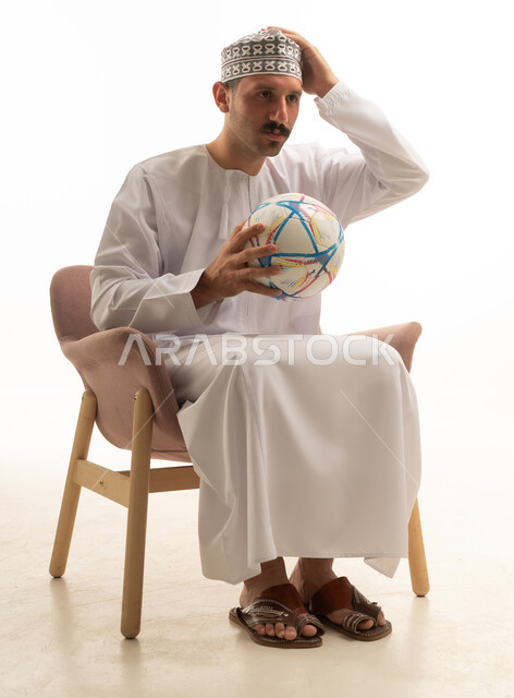 رجل عماني بالزي التقليدي يمسك كرة قدم