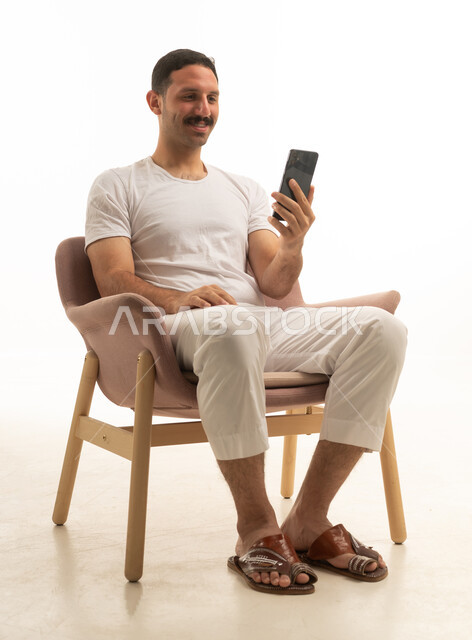 رجل سعودي يستخدم الهاتف الذكي جالساً على كرسي مريح