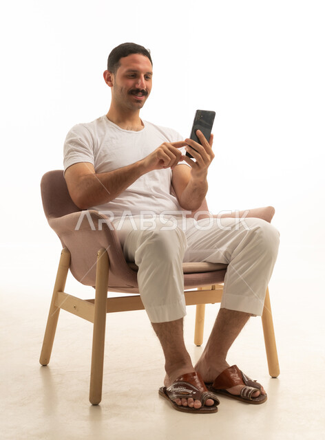 رجل سعودي يجلس على كرسي يستخدم الهاتف الذكي