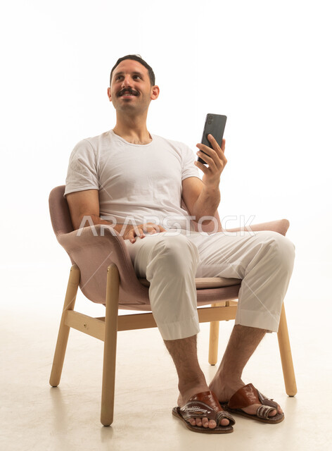 رجل سعودي يجلس على كرسي ممسكاً بهاتف ذكي