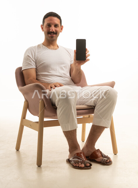 رجل سعودي يجلس حاملاً هاتفاً ذكياً في استوديو