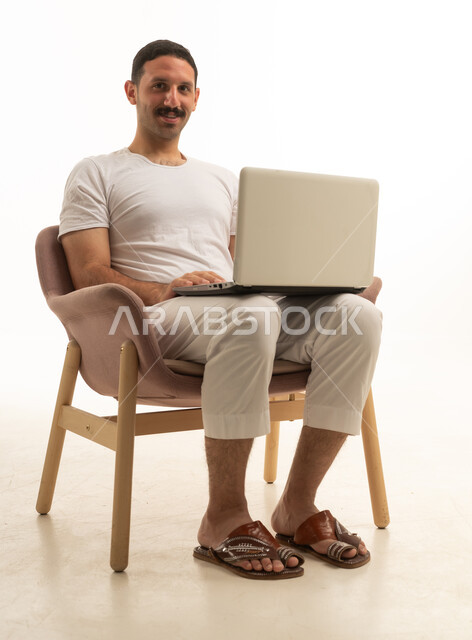 رجل سعودي يستخدم كمبيوتر محمول على خلفية استوديو بيضاء
