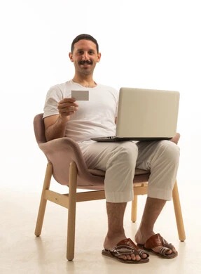 رجل سعودي  يجلس على كرسي يستخدم الحاسوب والبطاقة الائتمانية للتسوق