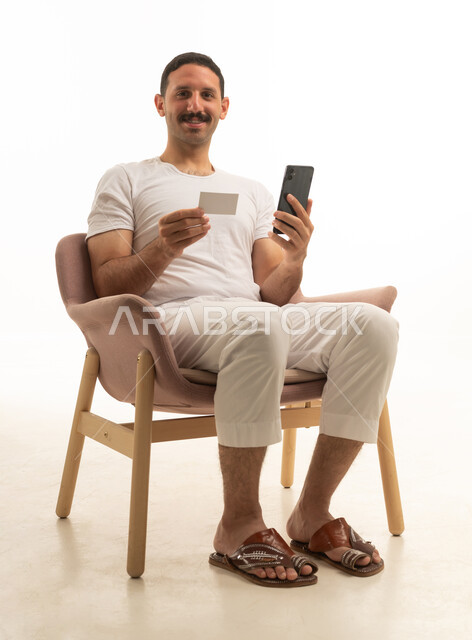 Saudi Man Using Credit Card and Smartphone on Chair