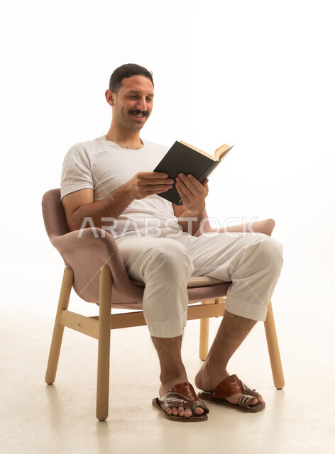 رجل سعودي يقرأ كتاباً على كرسي بخلفية بيضاء