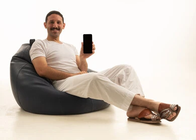 رجل سعودي يحمل هاتف ذكي على كرسي بين باج