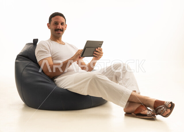 رجل سعودي يجلس على كرسي بين باج مع جهاز لوحي