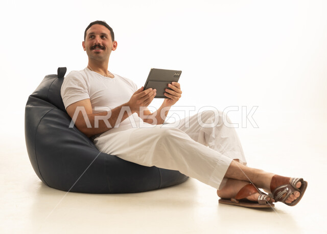 رجل سعودي يجلس على مقعد مريح ويستخدم تابلت في استوديو