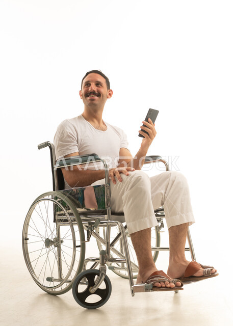 رجل سعودي على كرسي متحرك يحمل هاتف ذكي خلفية بيضاء