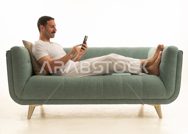 رجل سعودي يستخدم الهاتف الذكي على أريكة خضراء